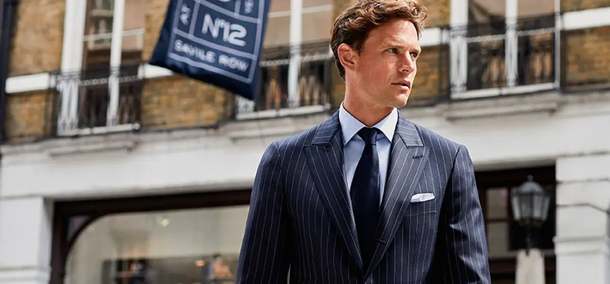 Scabal luxury suiting styled on Savile Row — man in navy pinstripe double-breasted suit by Holland & Sherry storefront
