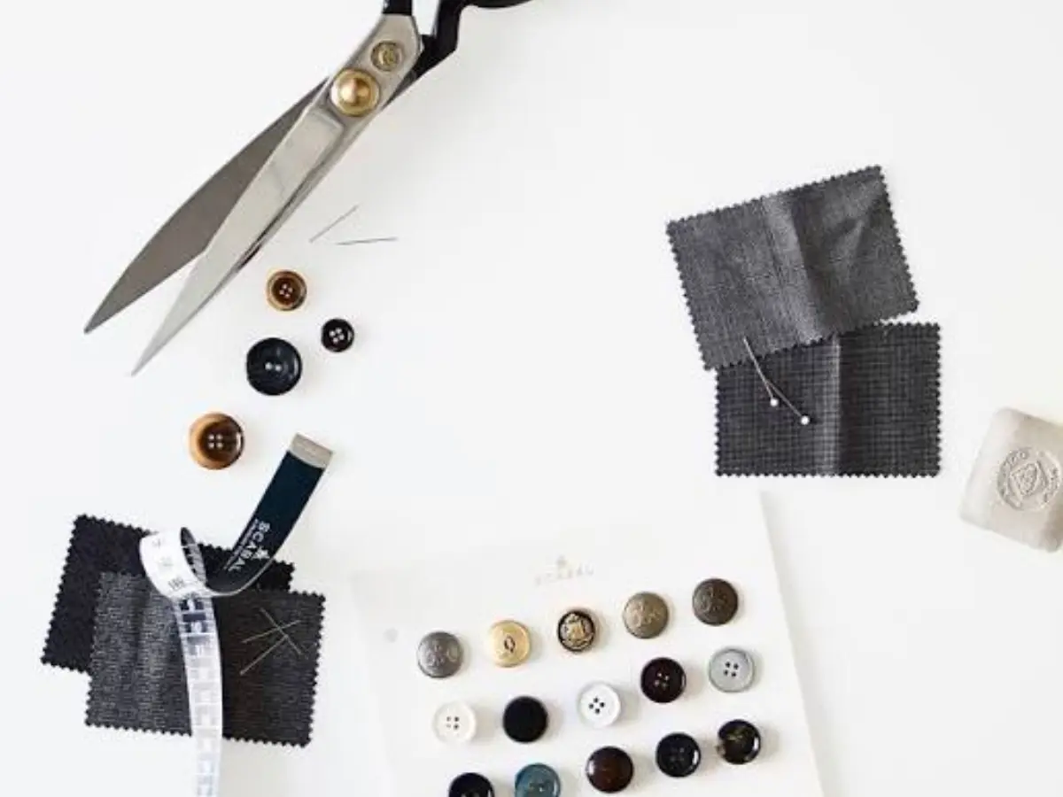 Scabal craftsmanship — shears, buttons, and wool fabric swatches on a cutting table