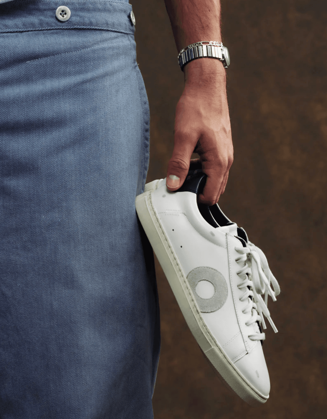 A person holding a white Oliver Cabell Low 1 sneaker with gray emblem, showcasing Italian calfskin leather and Margom sole craftsmanship.