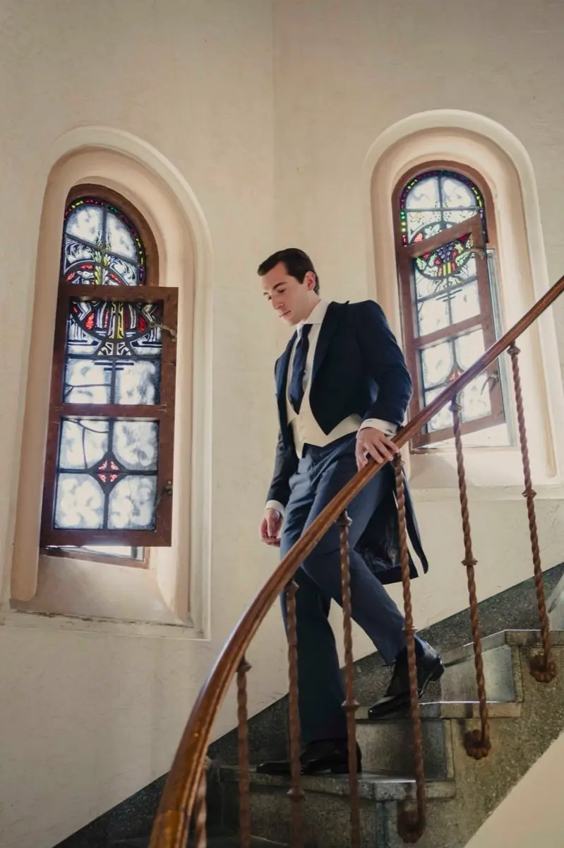 Man in custom tuxedo jacket with tails descending grand staircase at formal event