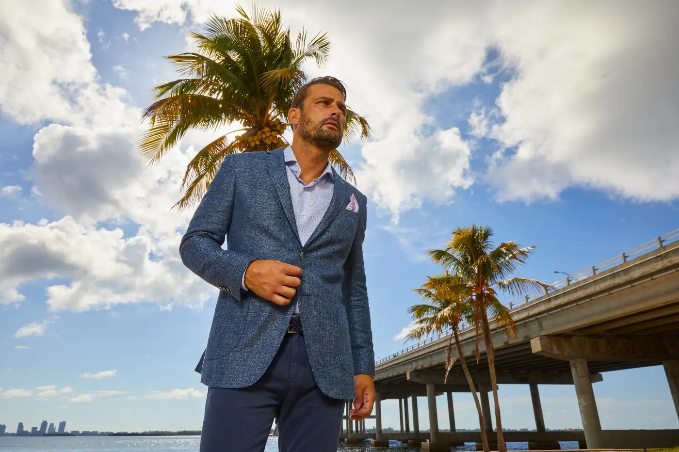 Man in a knit blue-grey blazer on a tropical bridge, resort wear fashion for Miami lifestyle