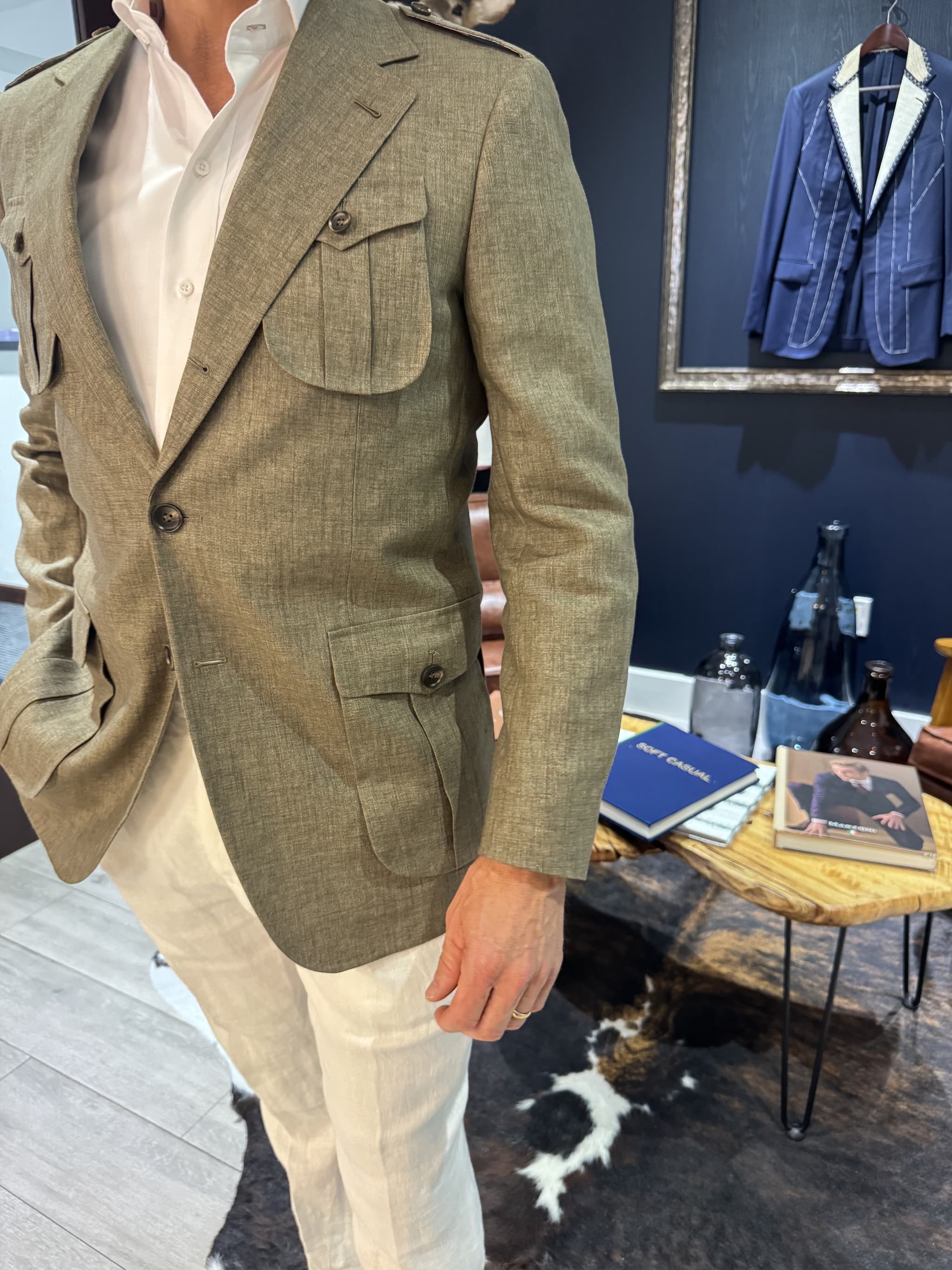 Man wearing an olive green safari style custom linen blazer with bellows pockets and epaulettes paired with white shirt and cream trousers.