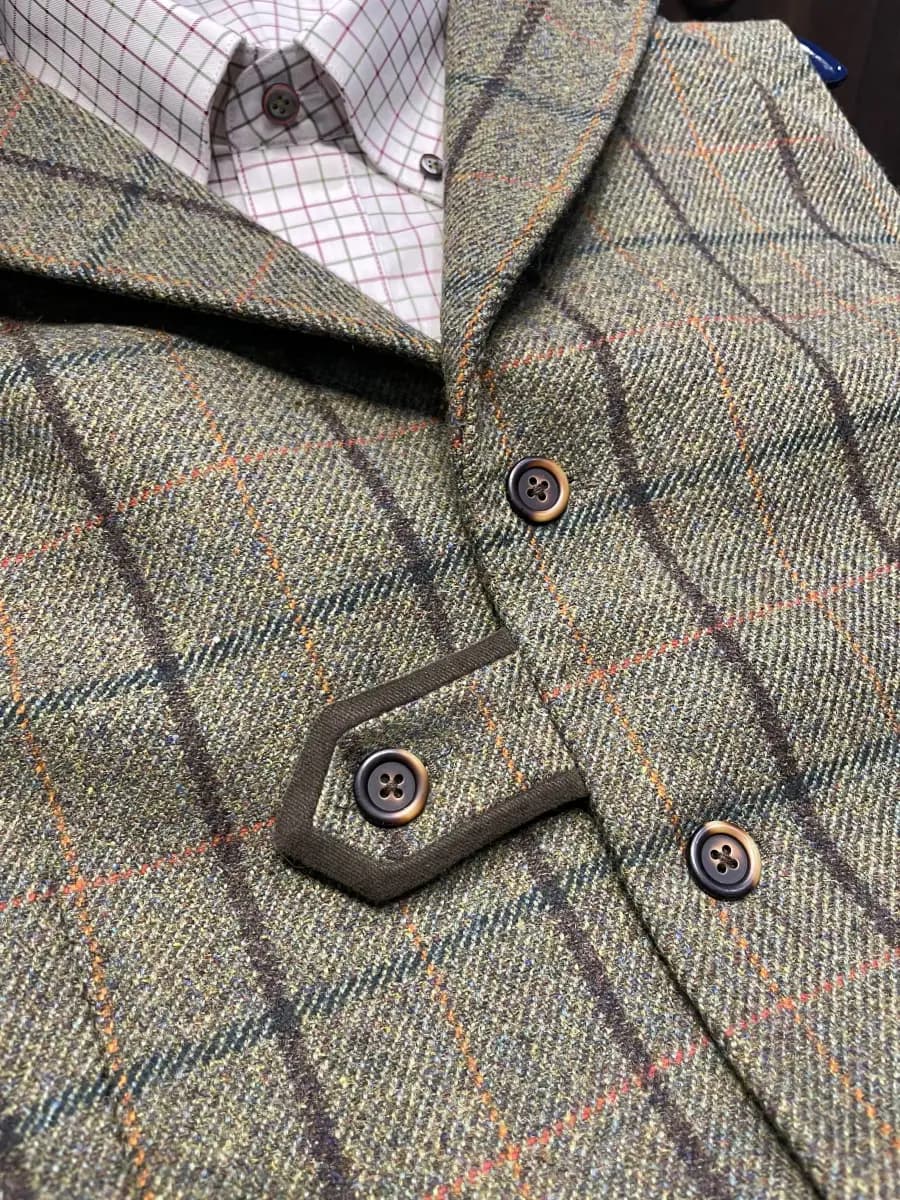 Custom green tweed shooting waistcoat with windowpane check, horn buttons, hexagonal cartridge pocket, and reinforced shoulder patches