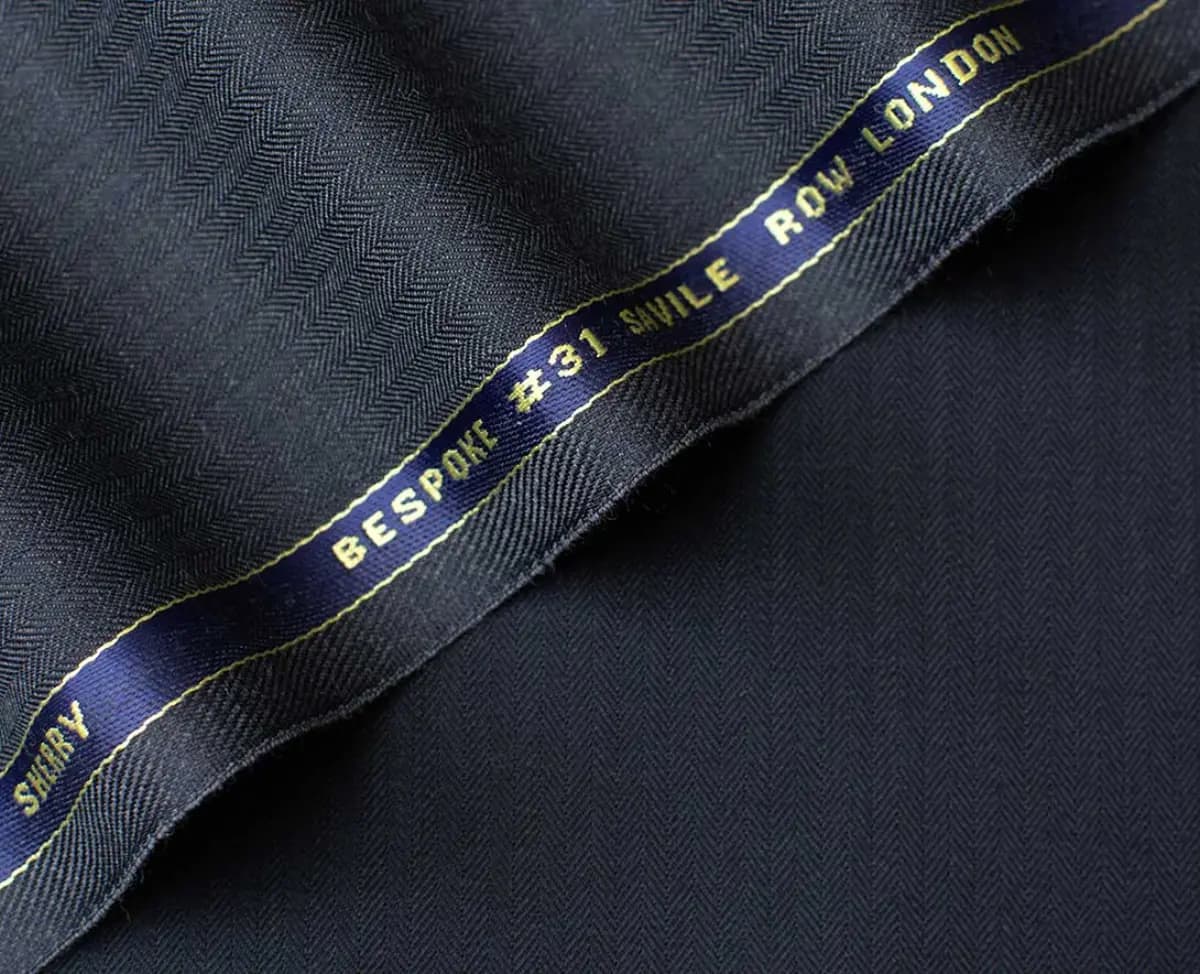 Holland & Sherry bespoke selvedge detail with gold woven label — herringbone wool suiting fabric