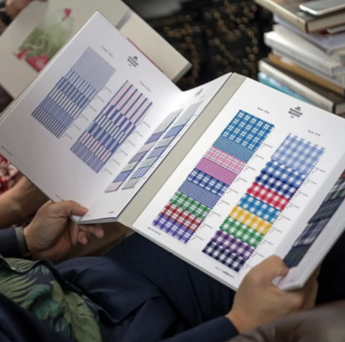 Thomas Mason swatch book open showing striped and checked shirting fabrics in a tailor's showroom