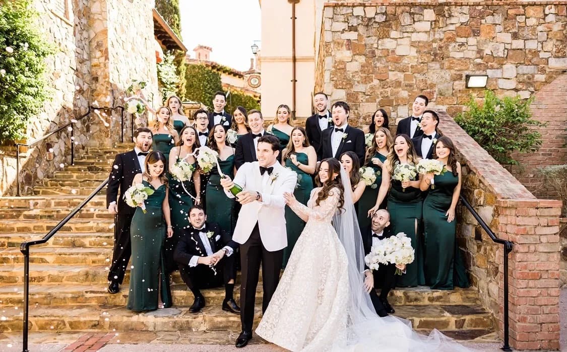 Wedding party celebrating with champagne on stone stairs by Bespoke By CB Miami