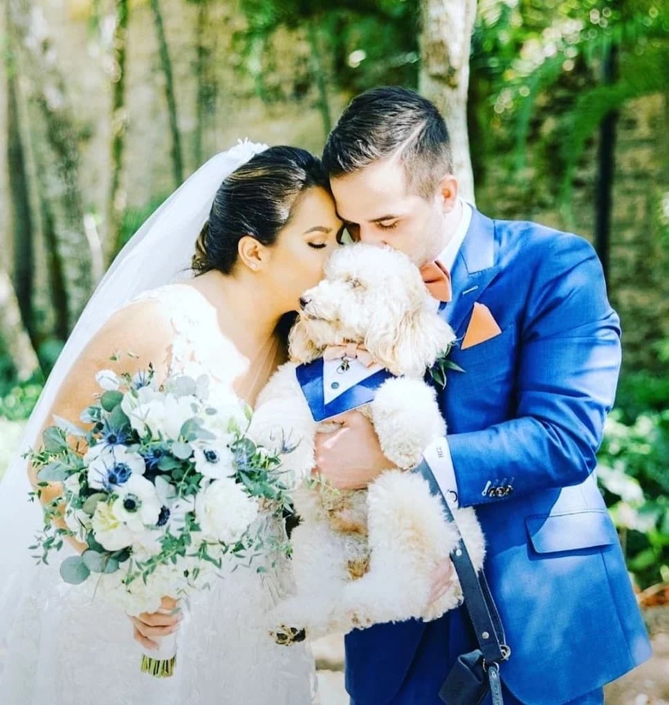 Groom in custom blue tailored wedding suit with rust bow tie beside bride and dog by Bespoke By CB Miami