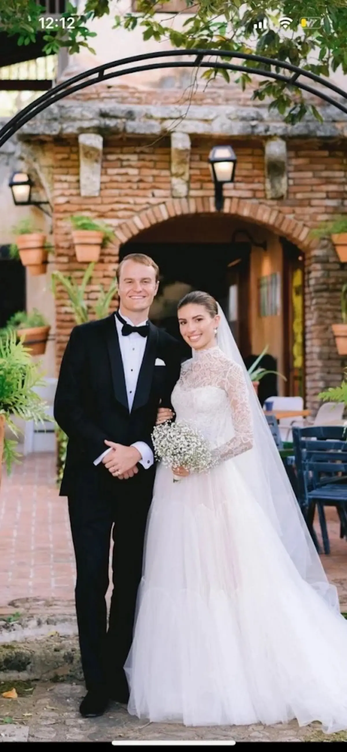Groom in custom black tuxedo with bride at brick archway wedding venue in Miami